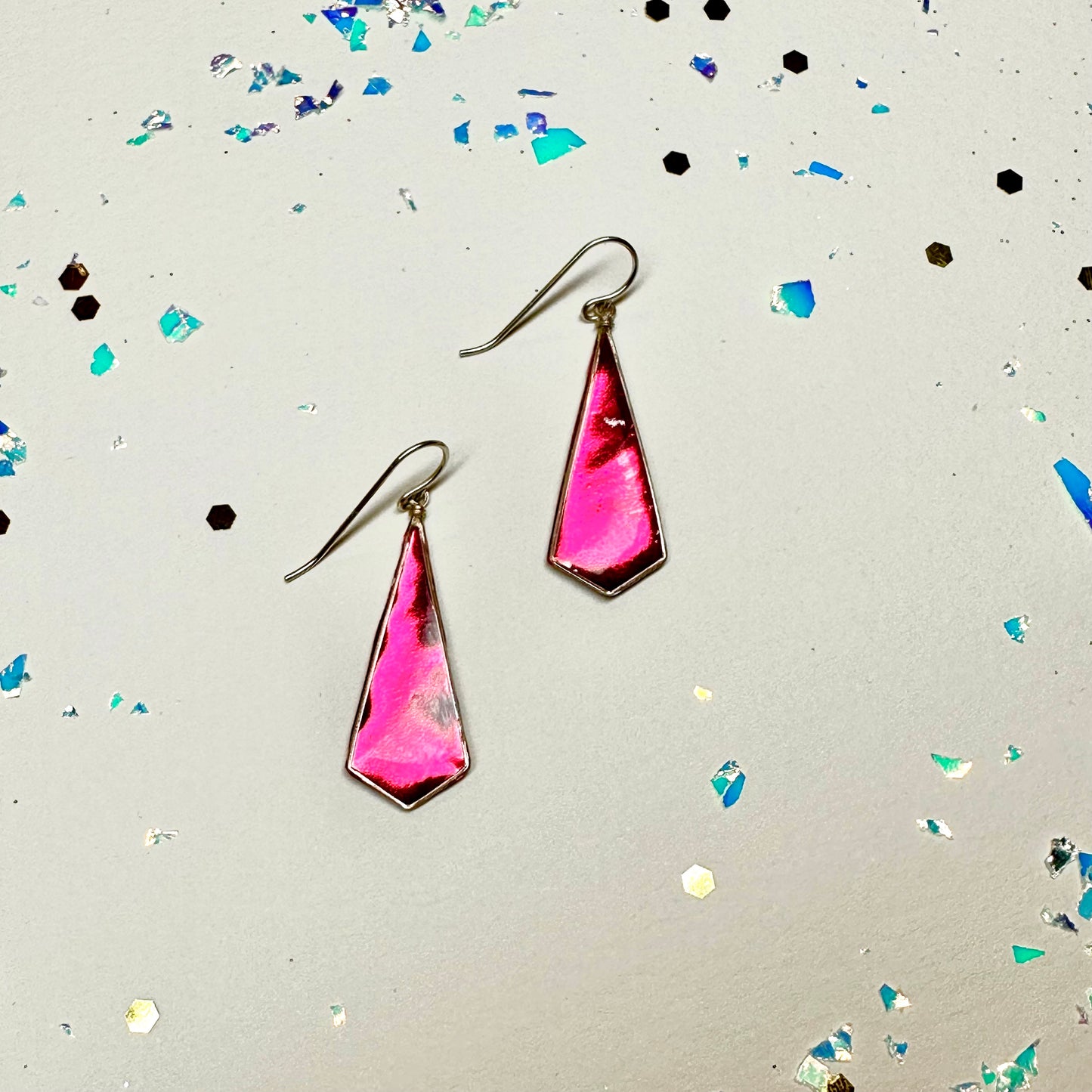 Sparkling party glitter borders the image and two beautiful handmade sterling silver earrings in barbie pink. shimmering metallic on a cream background.